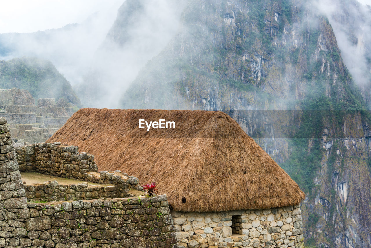 Thatched roof house against rocky mountains during foggy weather at machu picchu