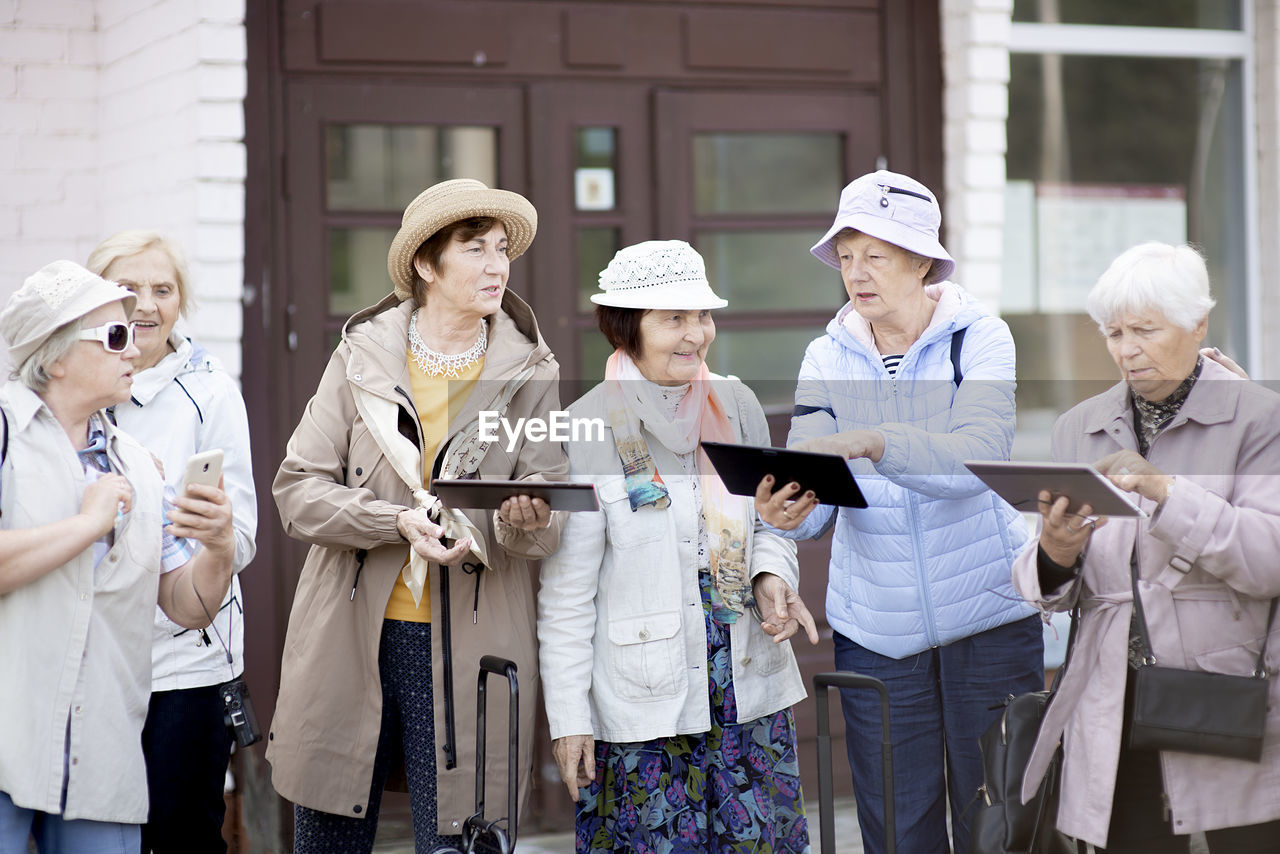 Group of senior elderly women looking at tablet on traveling journey during covid-19 pandemic.