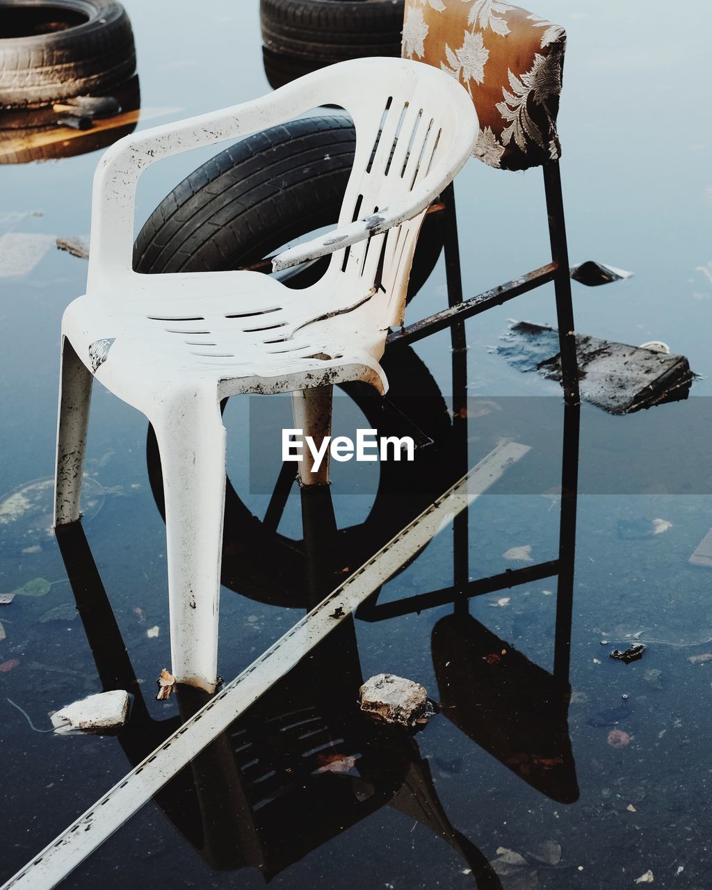 High angle view of abandoned broken white chair by tire in water