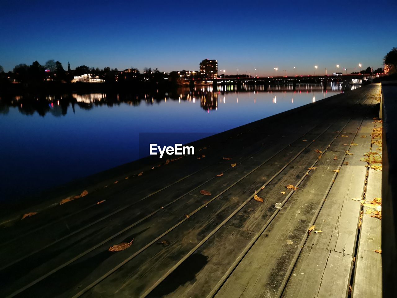 Illuminated city by river against clear sky at night