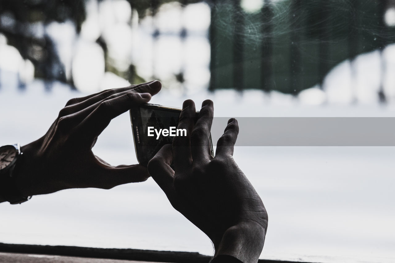 Cropped hands of man photographing by window