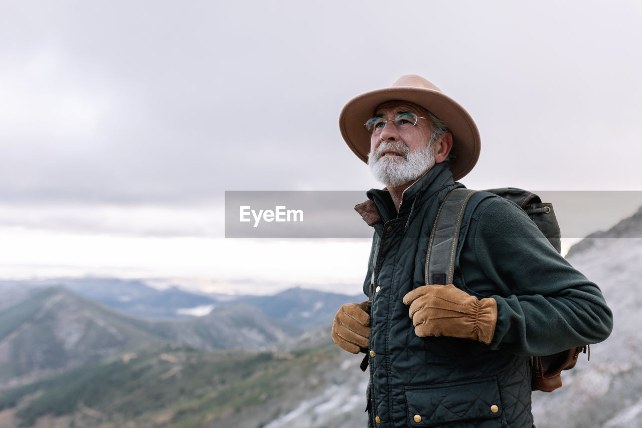 Side view of elderly male traveler with backpack standing in highlands in winter and admiring scenic landscape in caceres