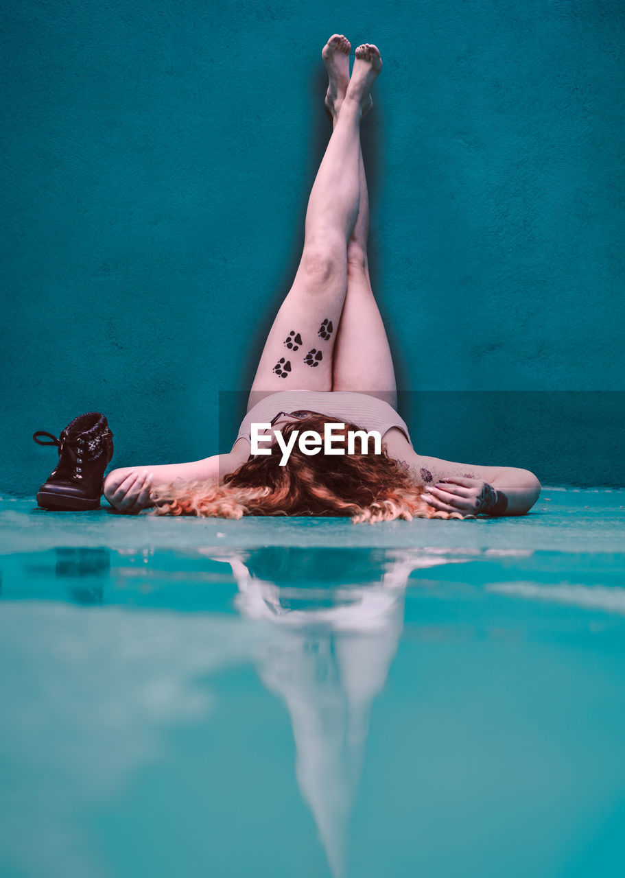 Young woman with feet up lying on turquoise wet floor