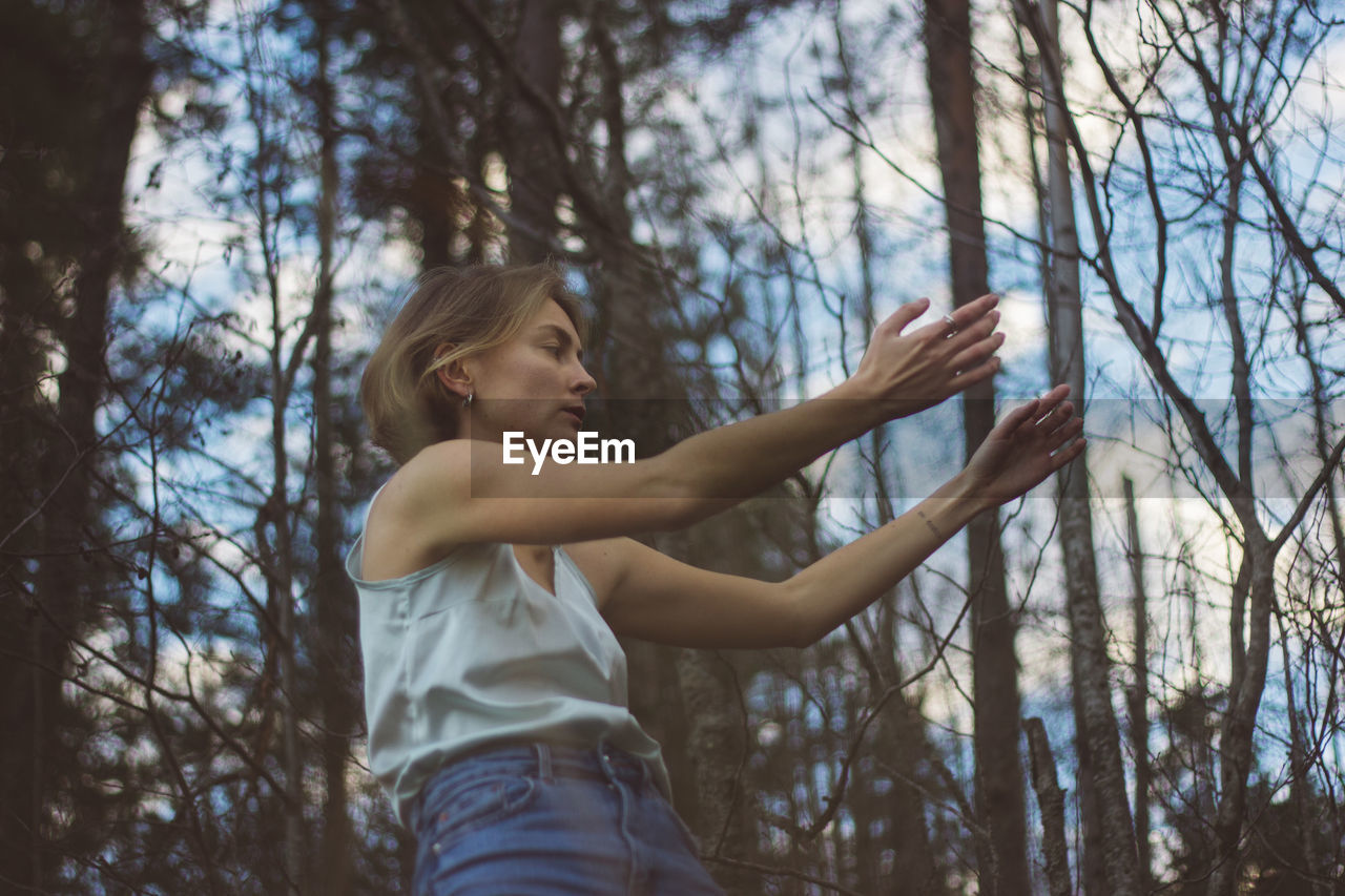 Low angle view of young woman dancing in forest