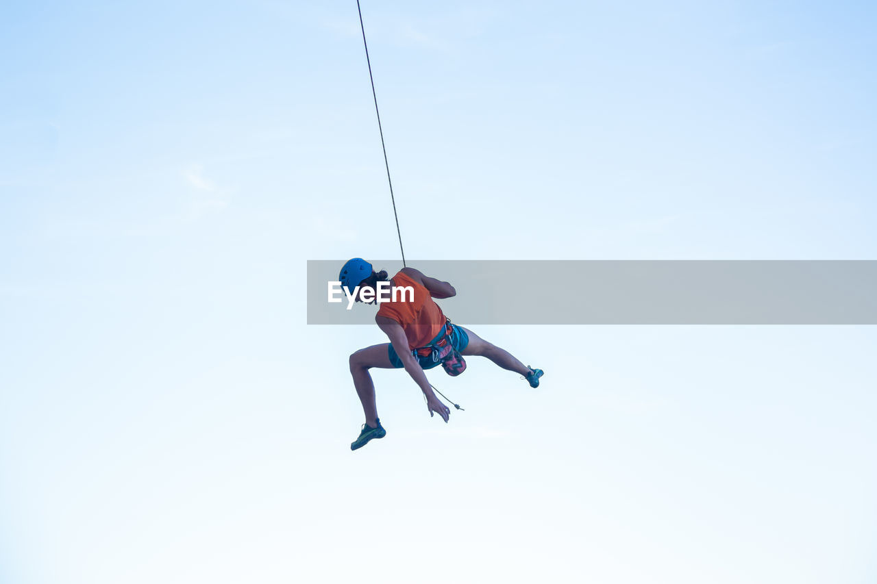 Low angle view of man swinging from rope against clear sky