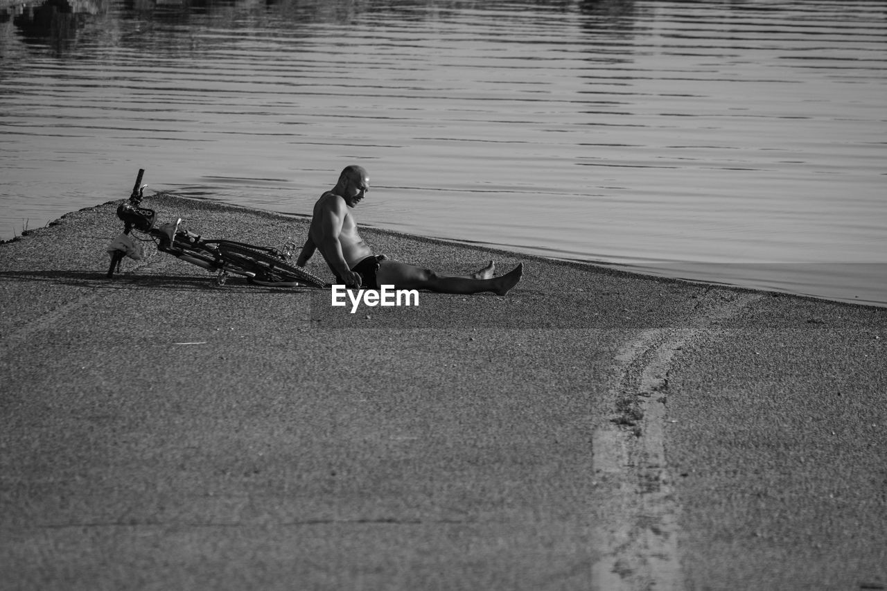 SIDE VIEW OF MAN SITTING BY LAKE