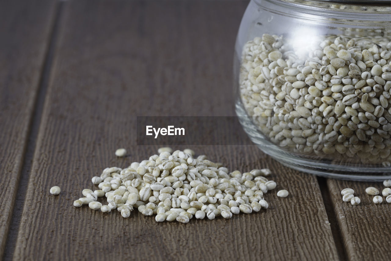 Close up on raw barley wheat with cooked barley water in glass over wooden background