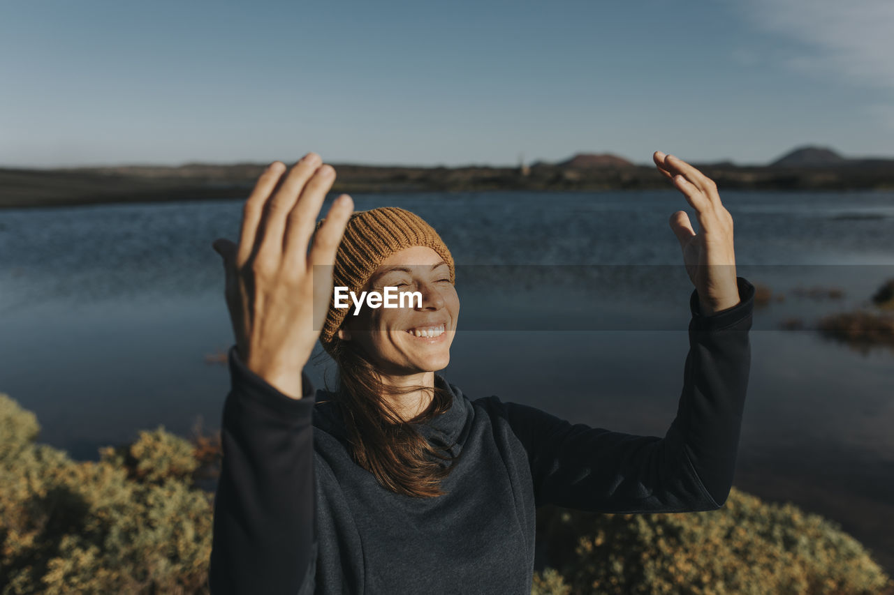 Happy woman with arms raised standing by lake