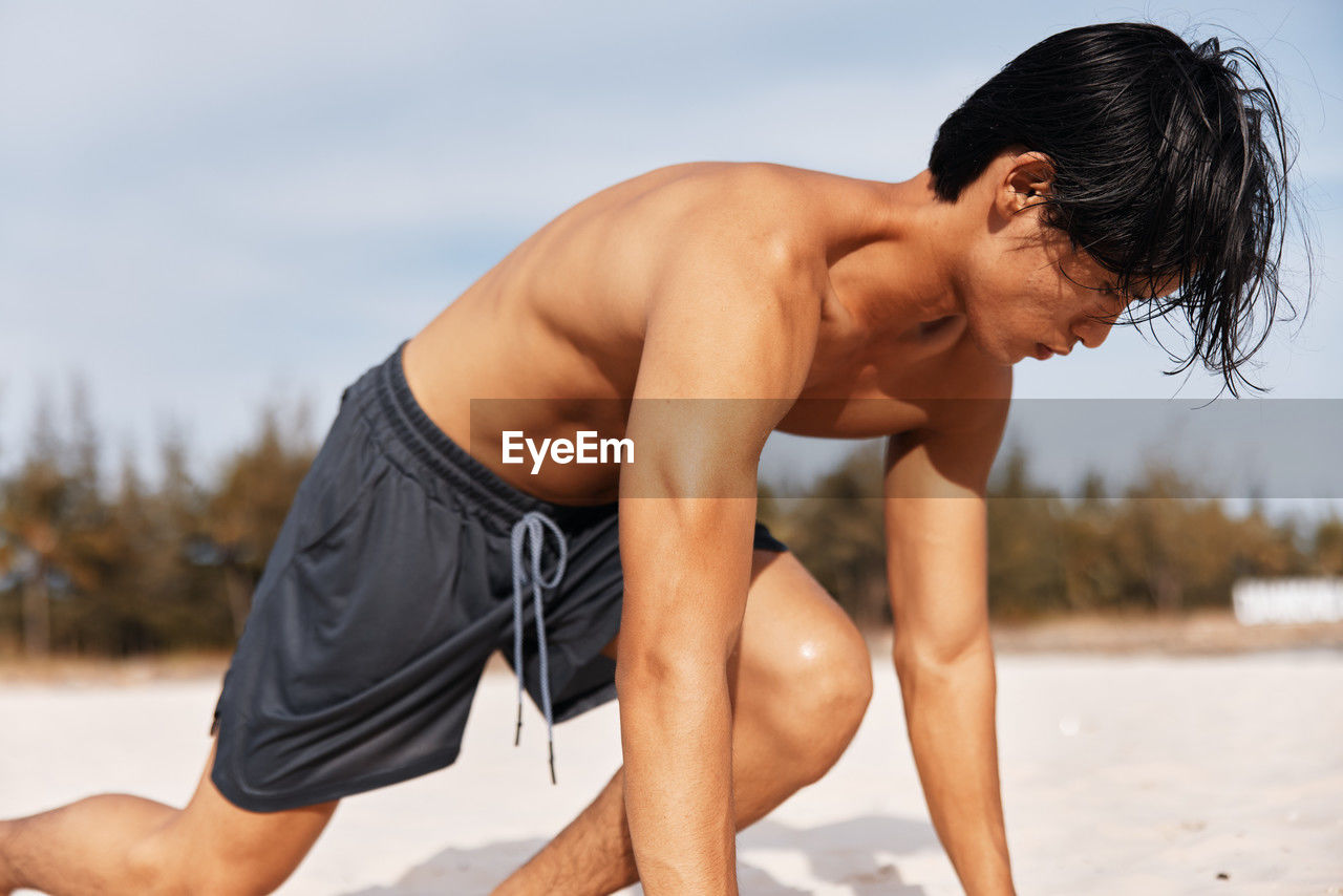 low angle view of shirtless man exercising at beach against sky