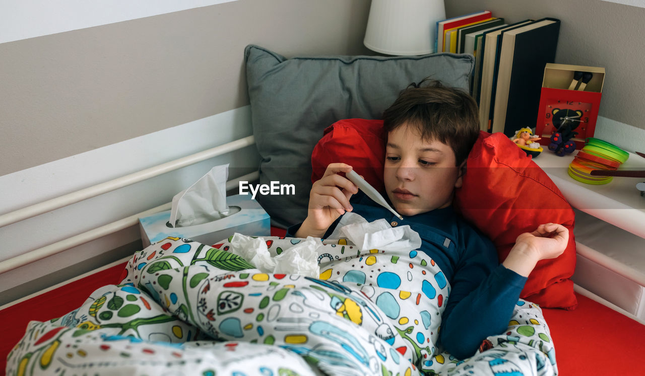 High angle view of boy holding thermometer on bed at home