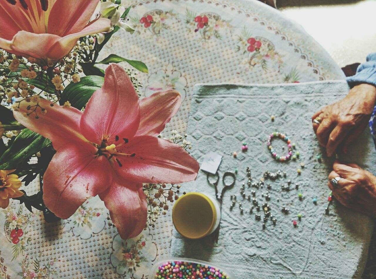 Cropped image of woman hands making art product on table by pink lilies