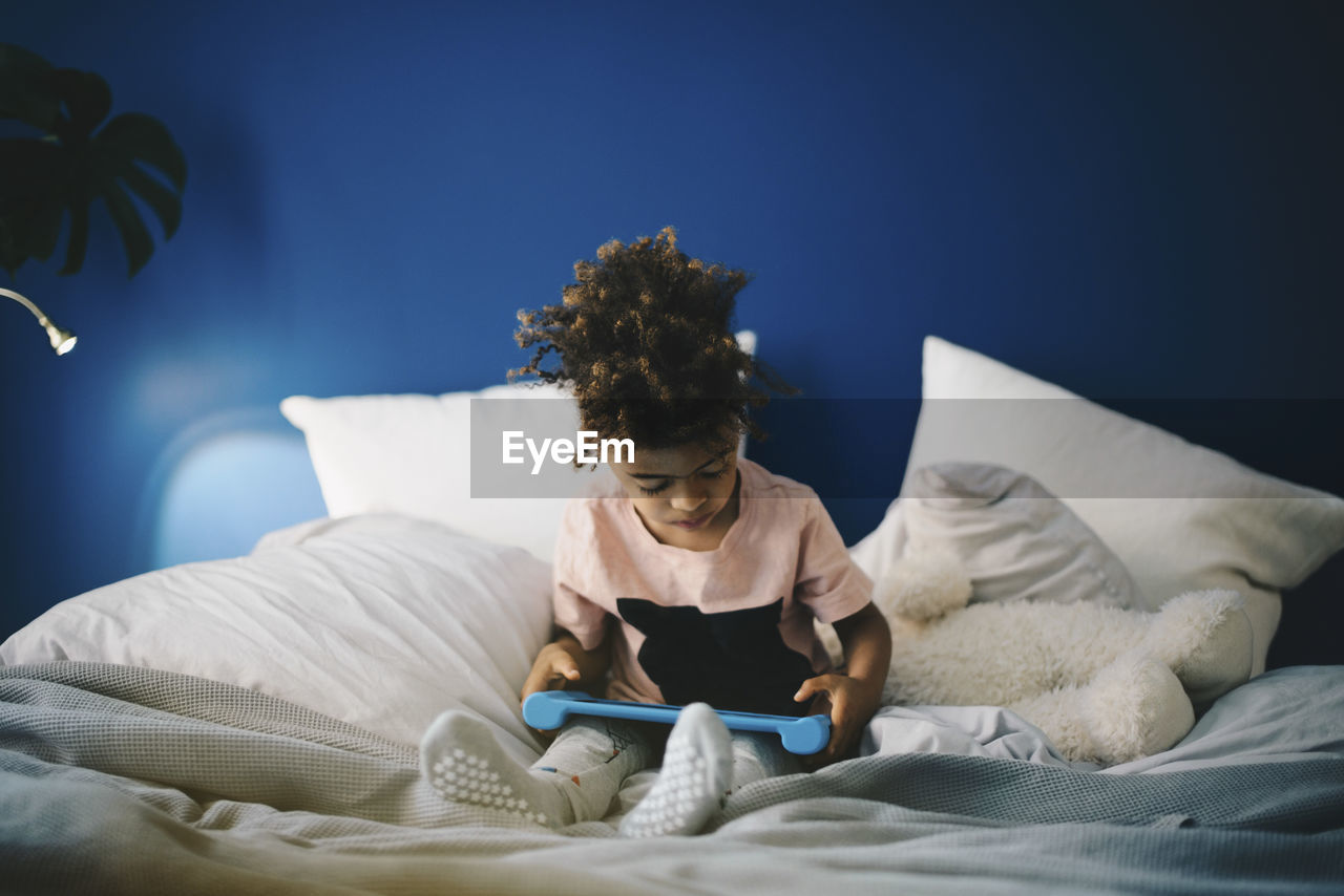 Boy using digital tablet while sitting on bed at home