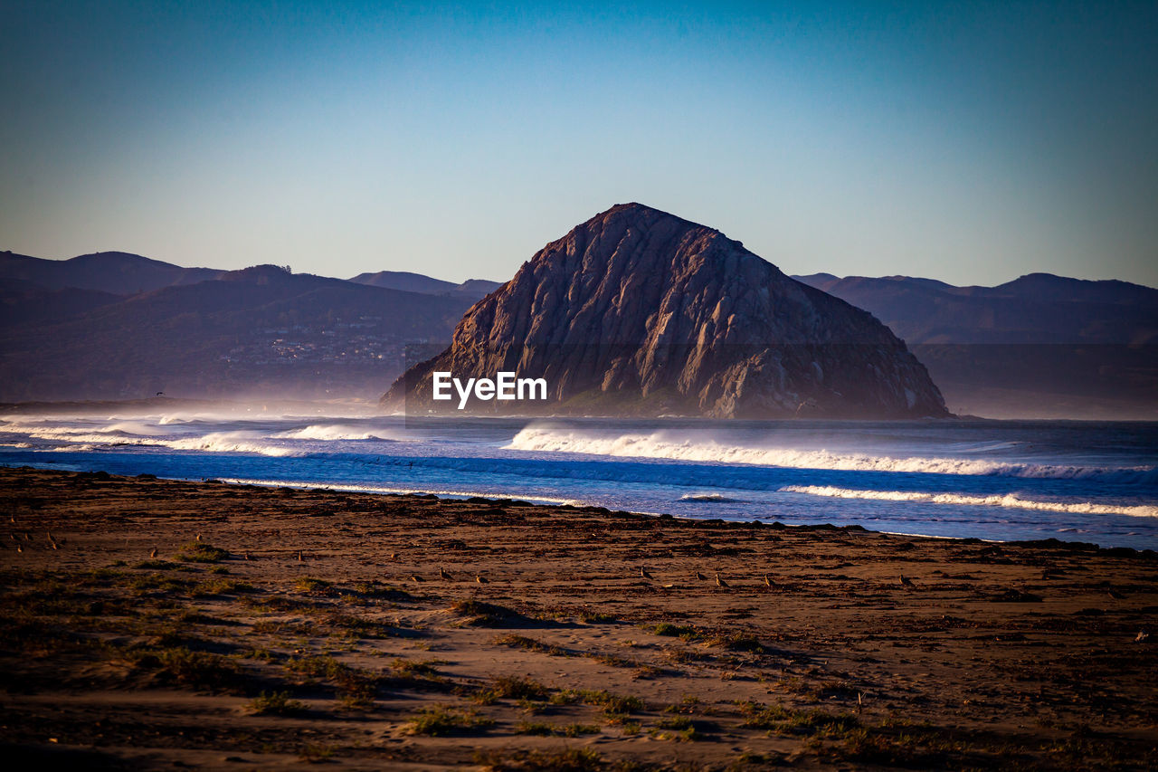 SCENIC VIEW OF SEA BY MOUNTAINS AGAINST CLEAR SKY