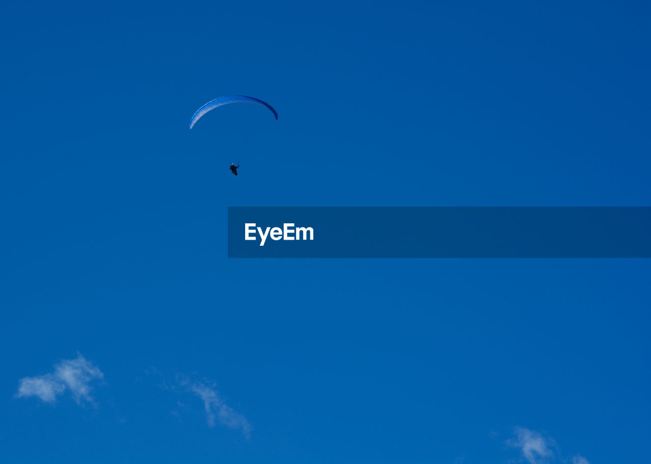 Low angle view of person paragliding against blue sky