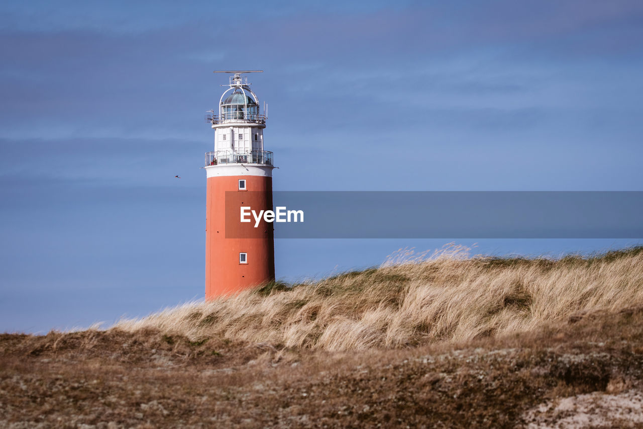 Lighthouse on field by building against sky