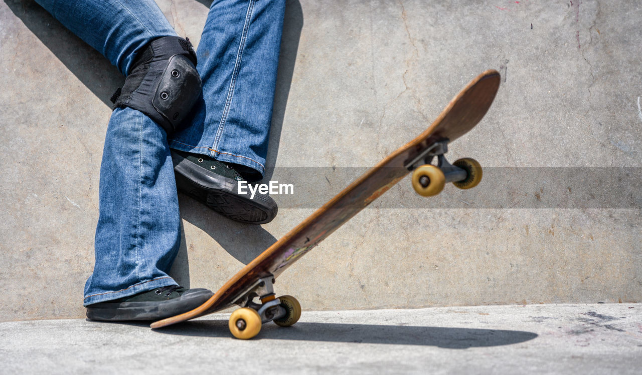 Low section of man with skateboard against wall