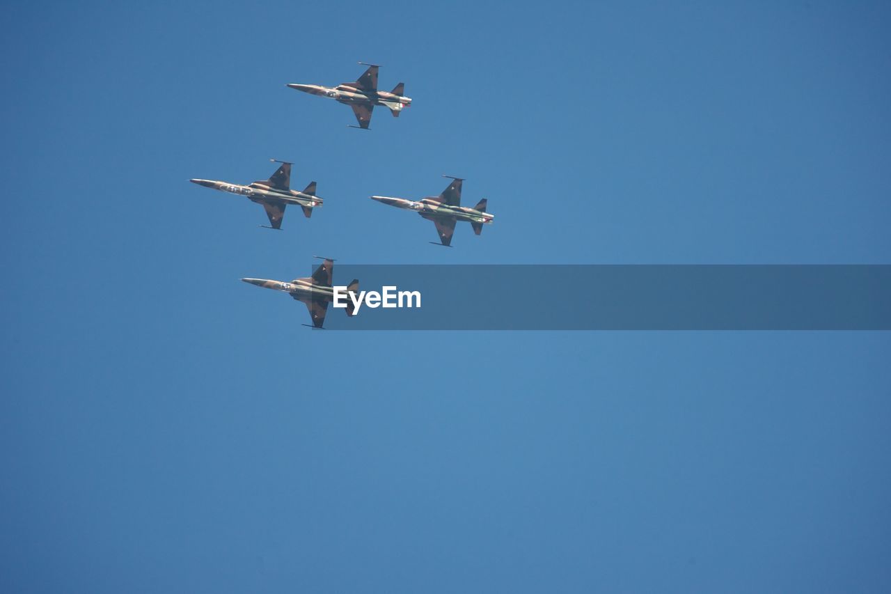 Low angle view of airplanes flying against clear blue sky