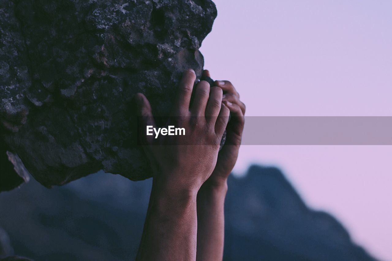 Close-up of hand holding rock against sky