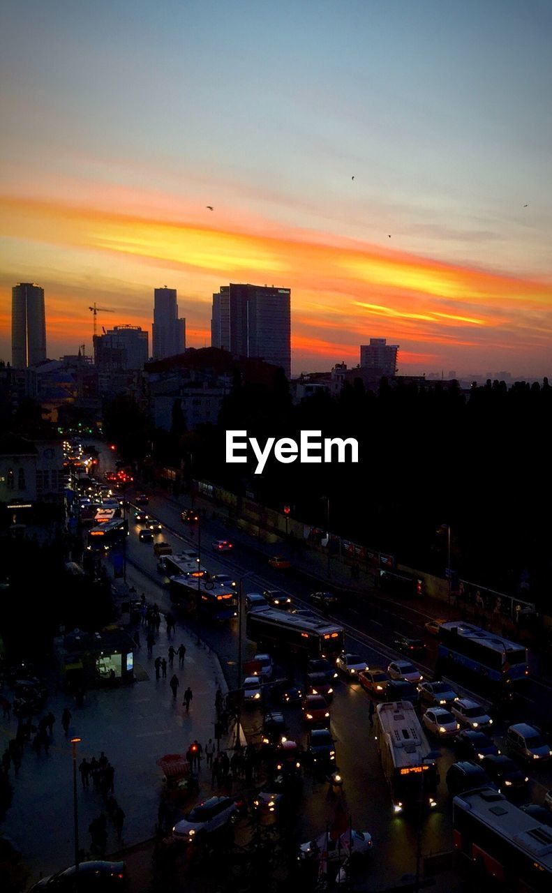 High angle view of illuminated street by silhouette buildings against sky during sunset