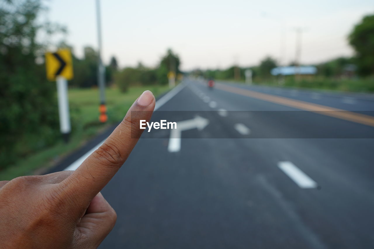 Cropped image of person hand on road against sky