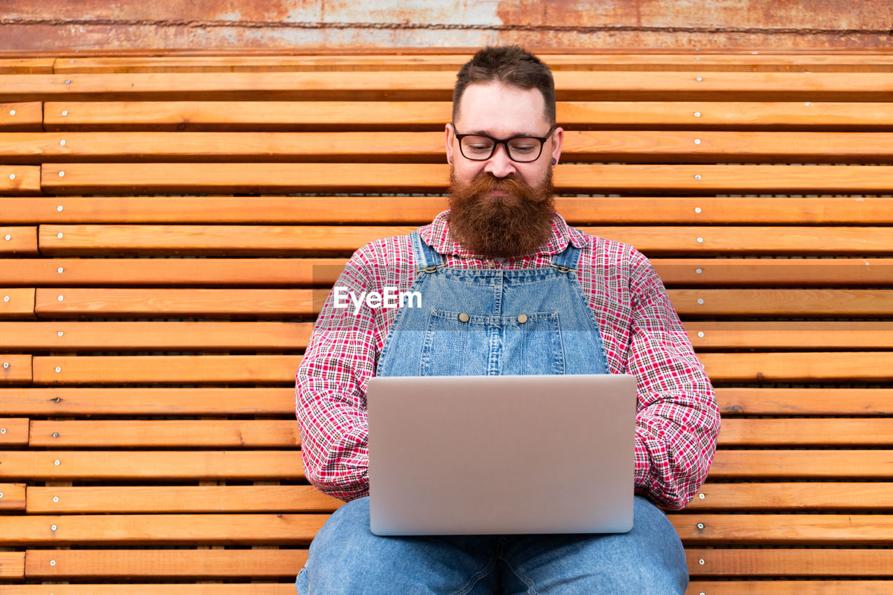 Focused bearded hipster man freelancer using laptop, writing email or message, chatting, shopping.