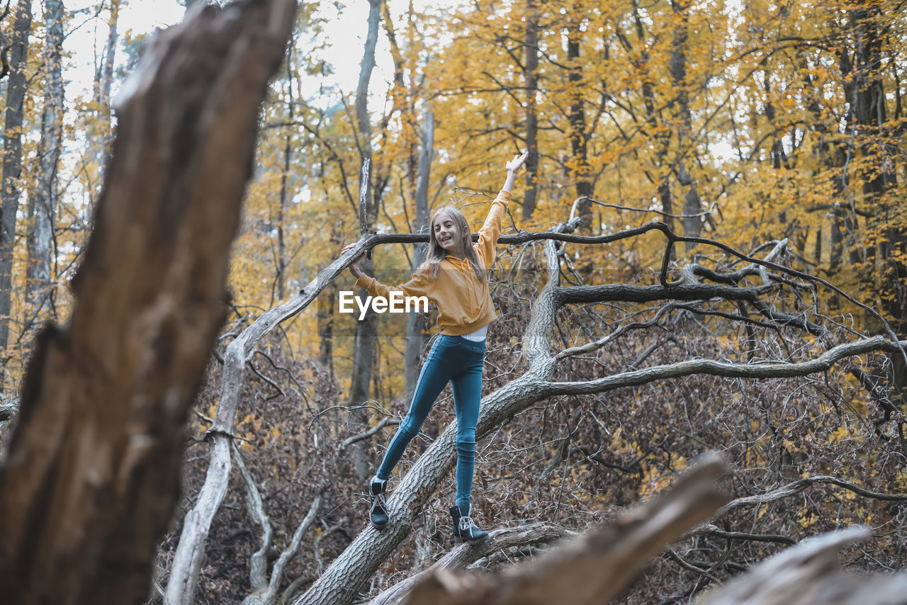 Full length of girl standing on tree trunk in forest