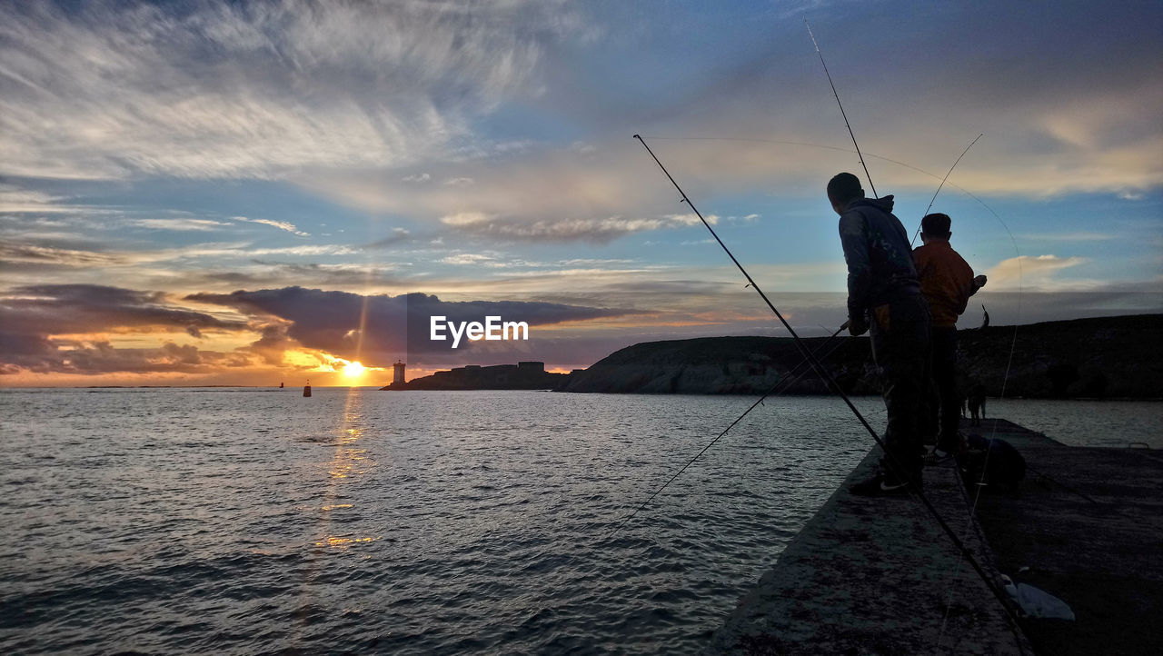 SILHOUETTE MAN FISHING IN SEA AGAINST SUNSET SKY