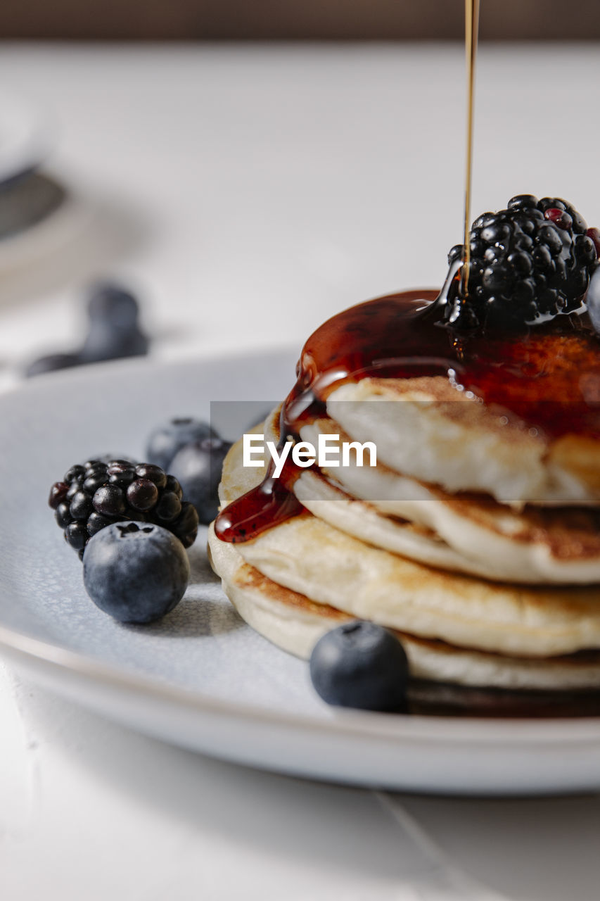 Close up of syrup pouring down a stack of pancakes with berries on top