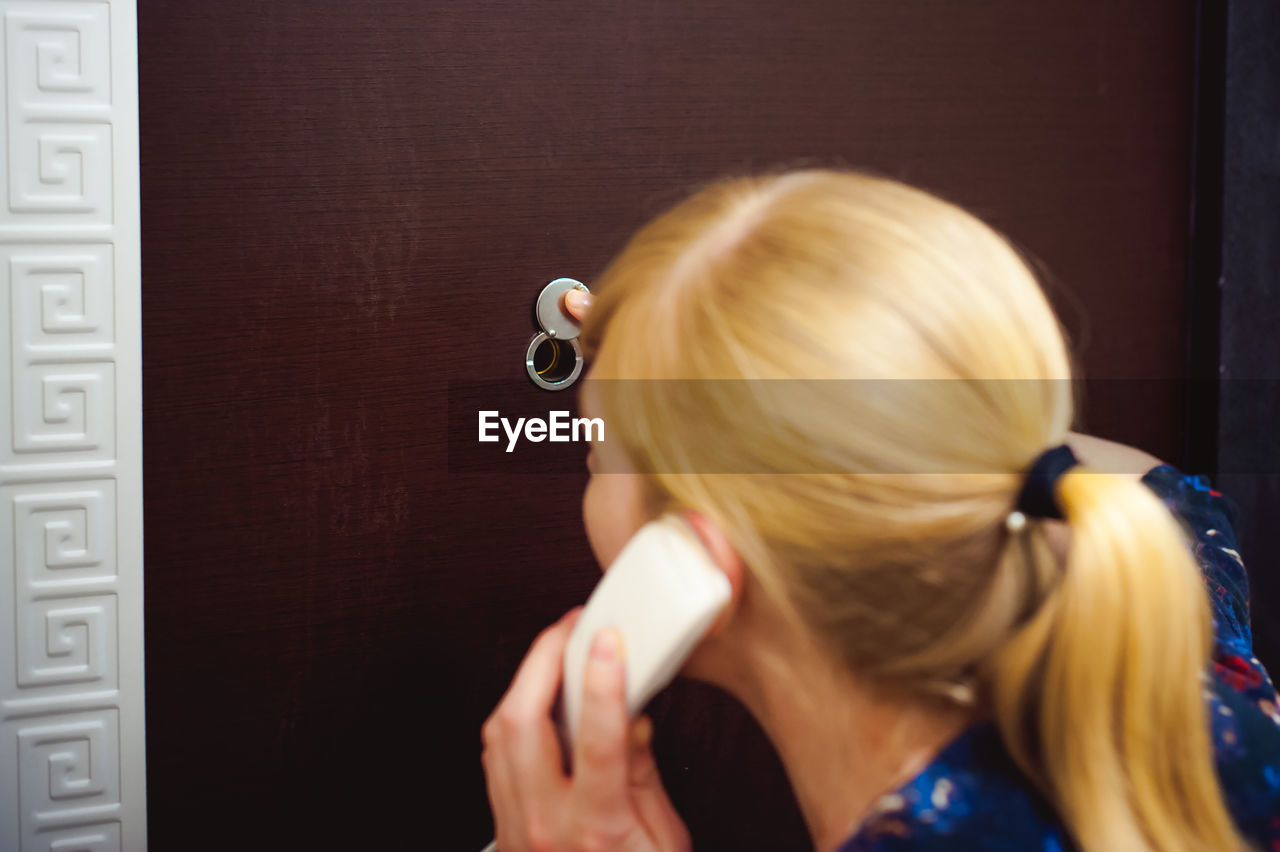 Rear view of woman talking on telephone while standing against door