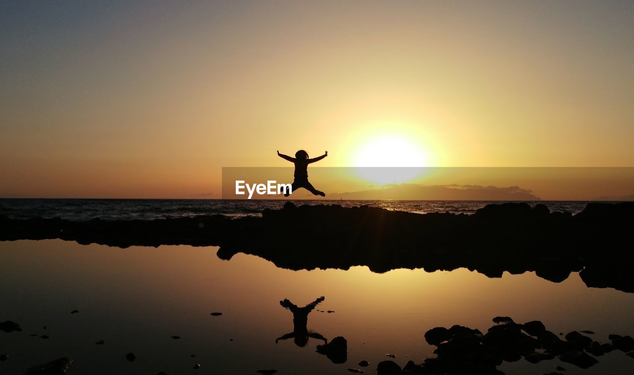 Silhouette man jumping at beach against sky during sunset