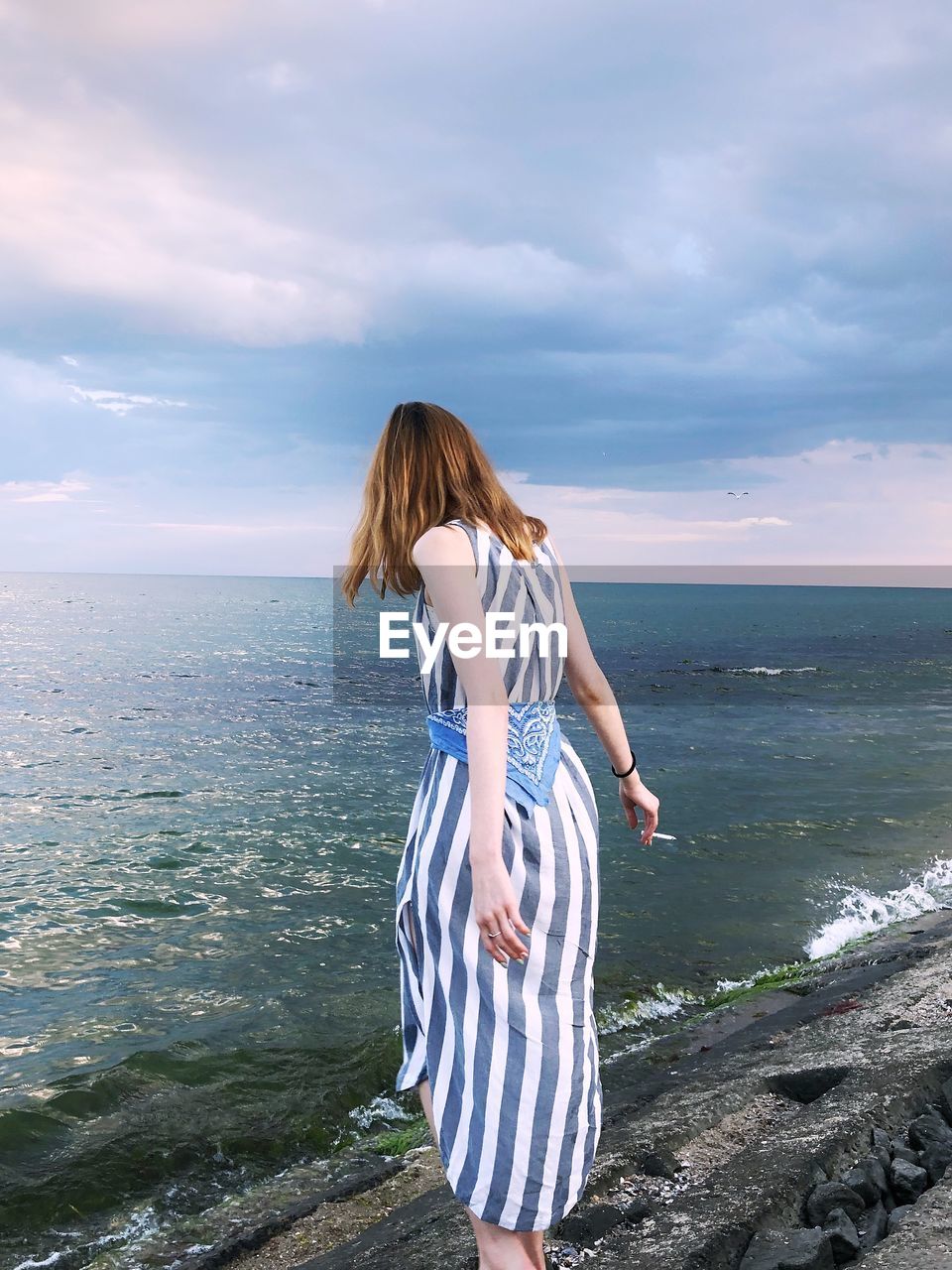 Rear view of woman standing by sea against sky