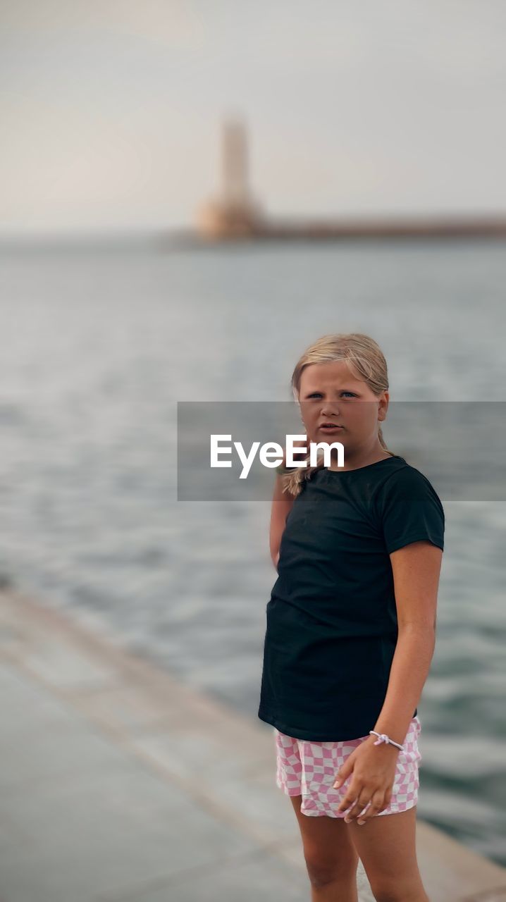 Portrait of young girl standing by sea against sky