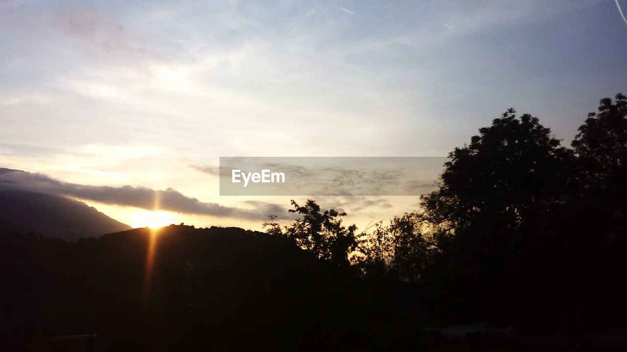 Silhouette trees and mountain against sky during sunrise