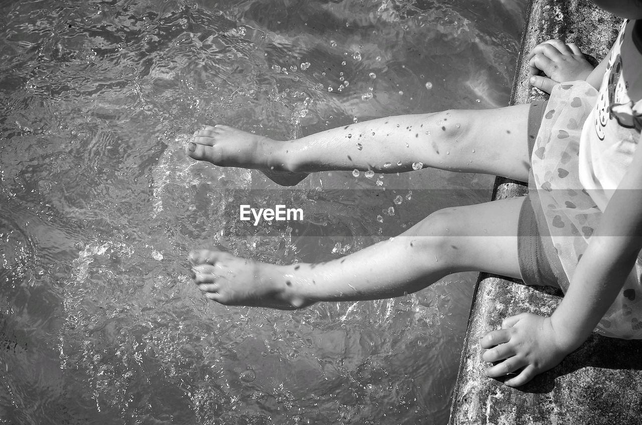 Low section of playful girl sitting on jetty by river