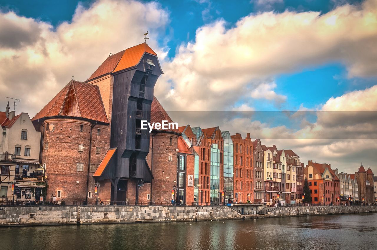 BUILDINGS WITH WATERFRONT AGAINST CLOUDY SKY