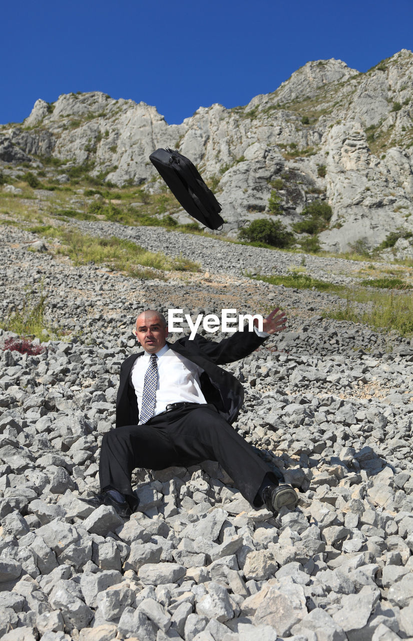 FULL LENGTH OF MAN SITTING ON ROCK IN SUNLIGHT