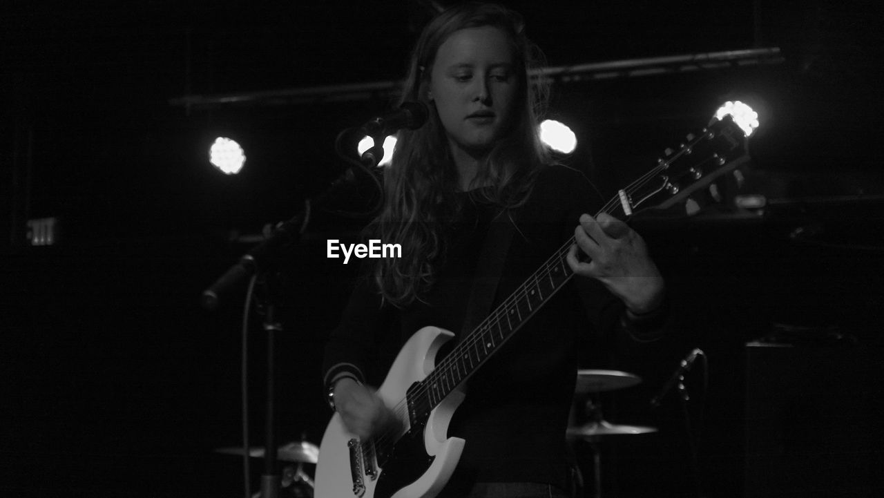 Young musician playing guitar on stage at nightclub