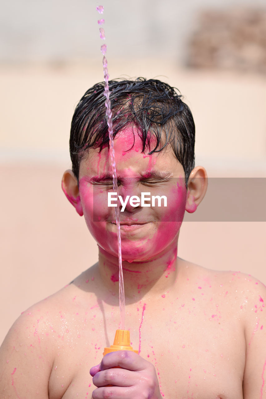 Shirtless boy playing with squirt gun during holi