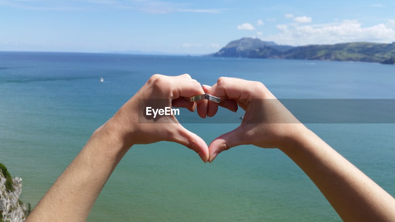 CLOSE-UP OF HANDS HOLDING HEART SHAPE AGAINST SEA