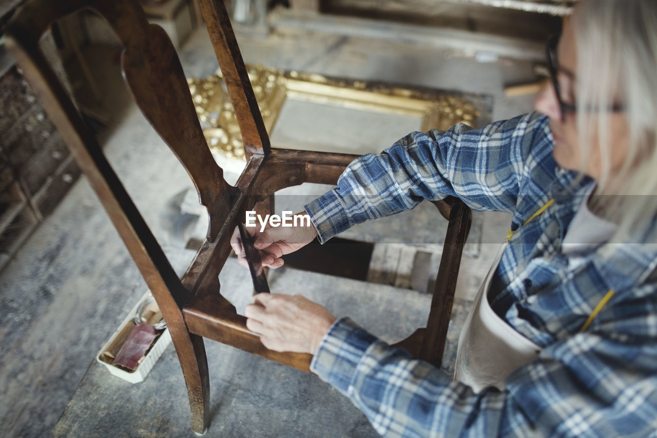 High angle view of craftsperson making wooden chair at workshop