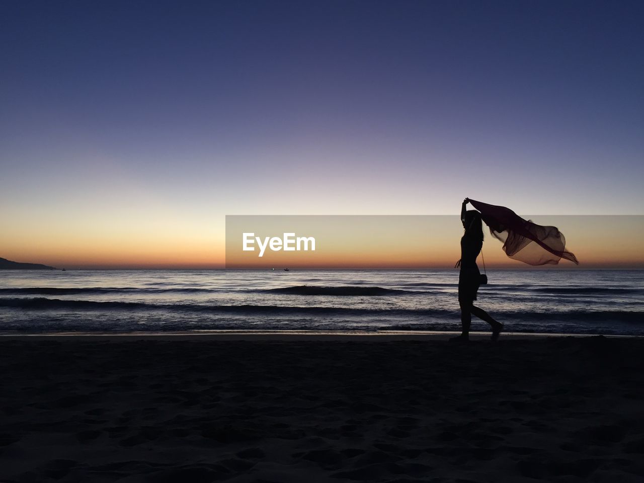 Woman with fabric running on beach against clear sky