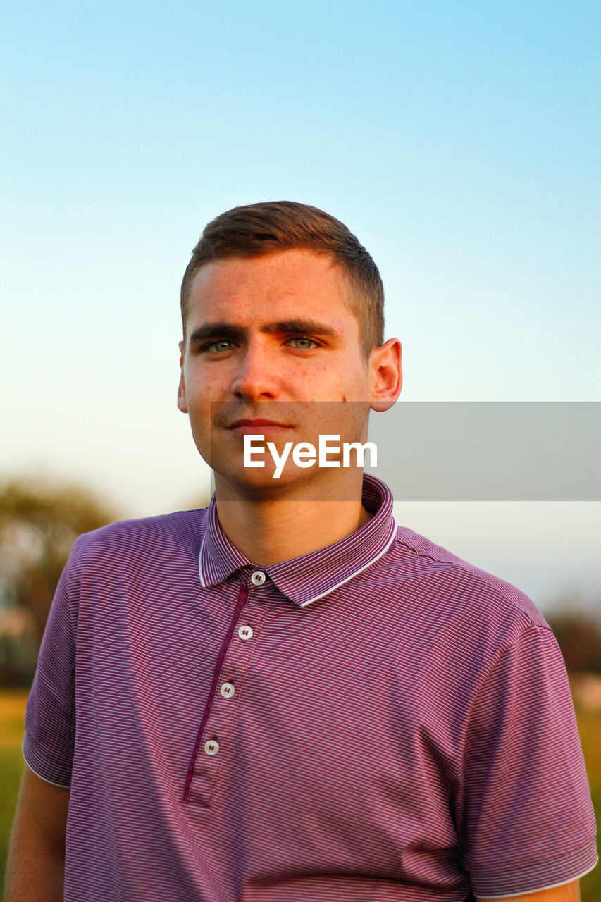 Young people.portrait of serious young brunette man in purple polo shirt standing outdoor on nature 