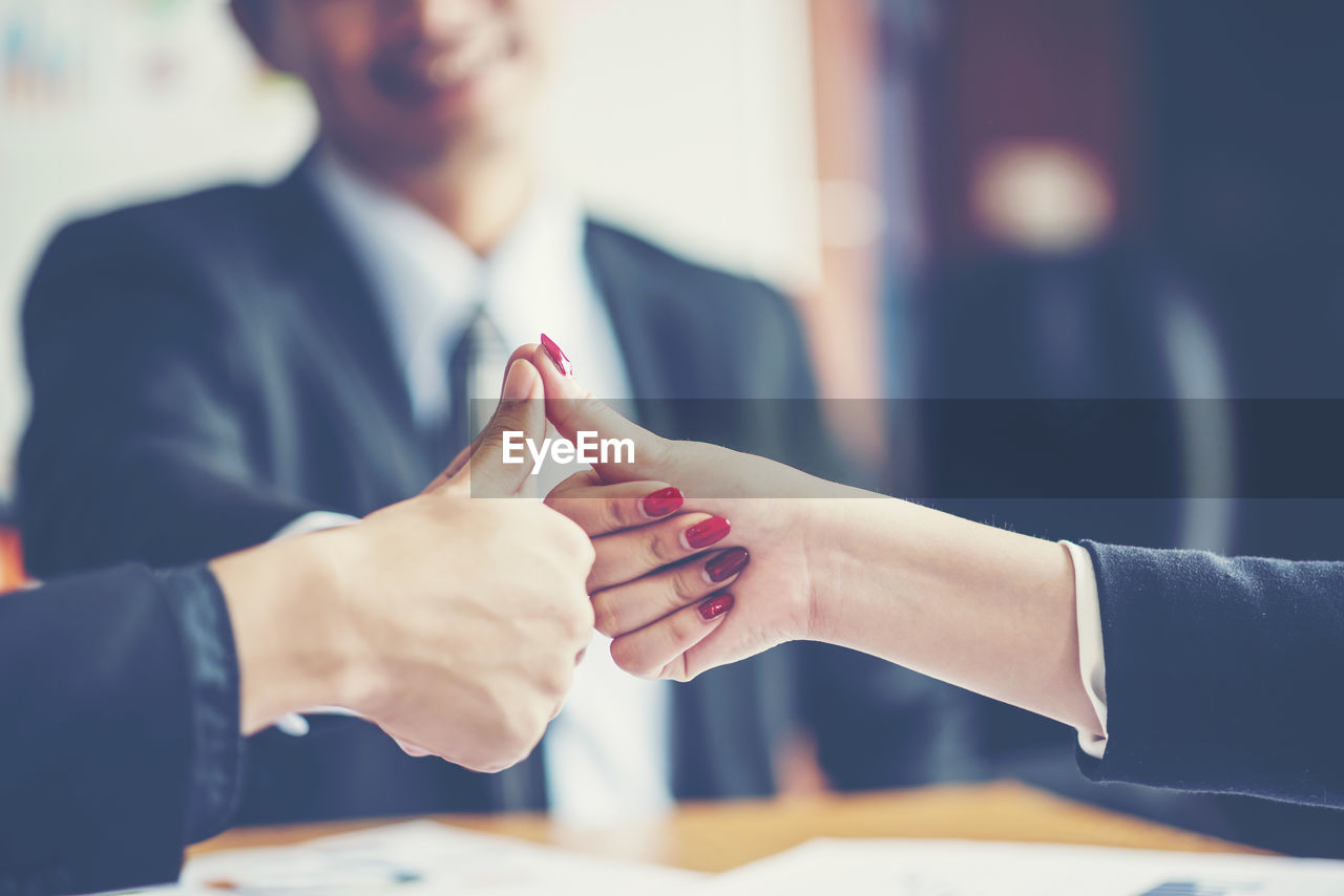 Close-up of business colleagues gesturing thumbs up in office