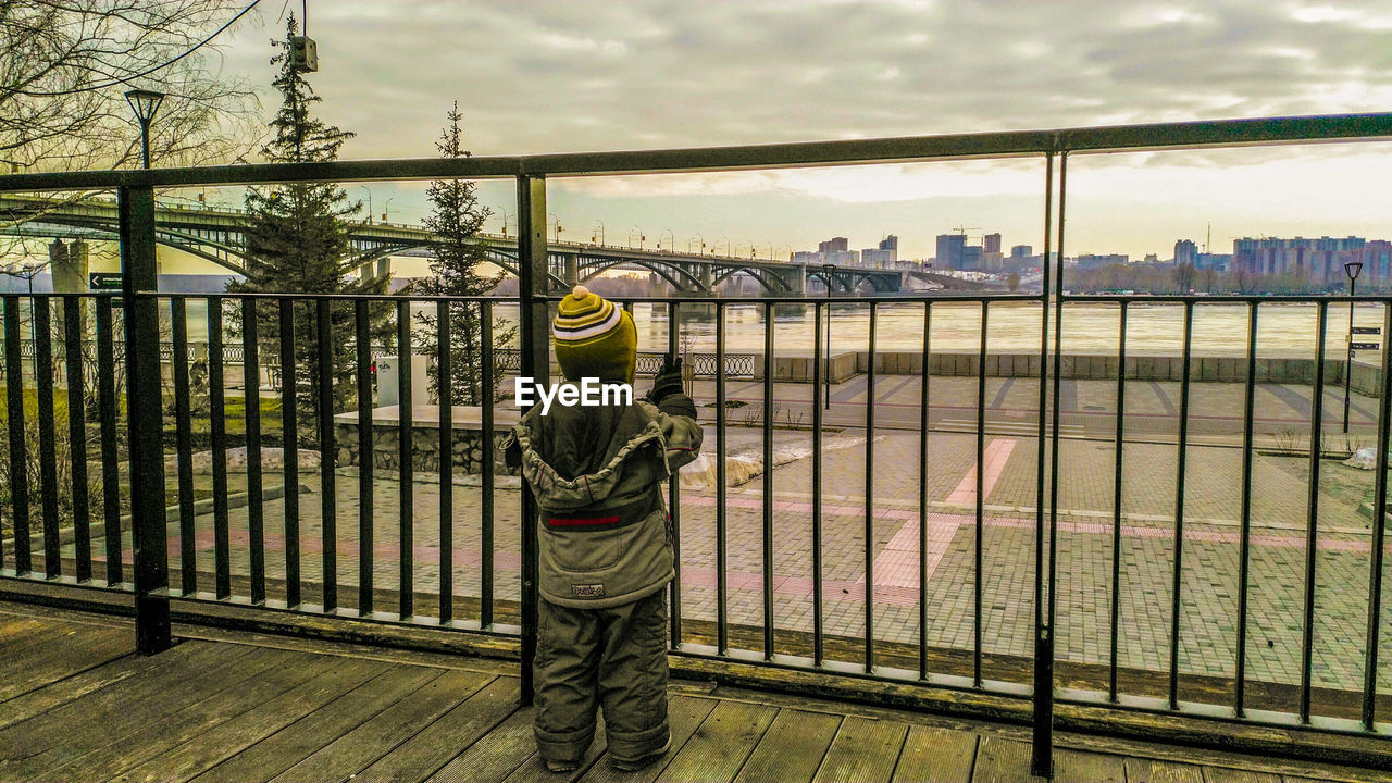 Rear view of man standing by railing against sky