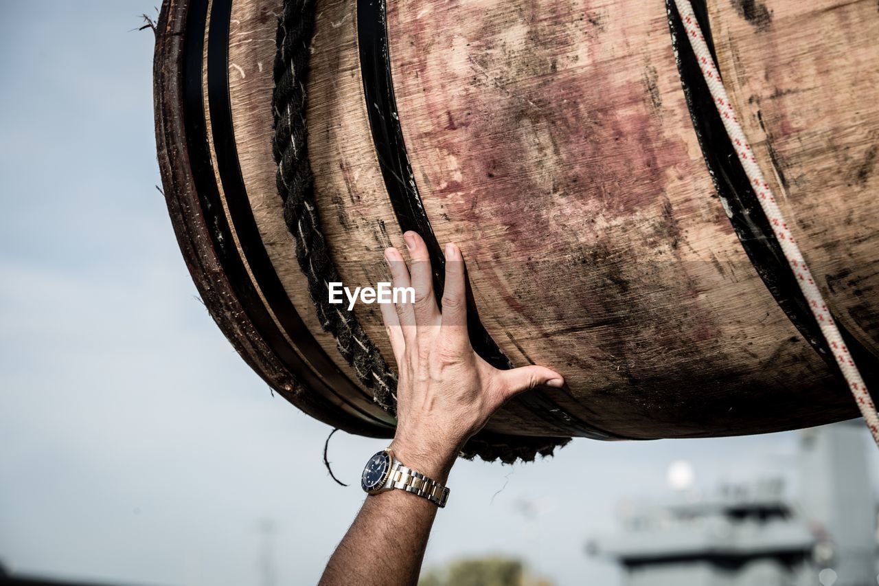 Close-up of hand touching wooden barrel against sky