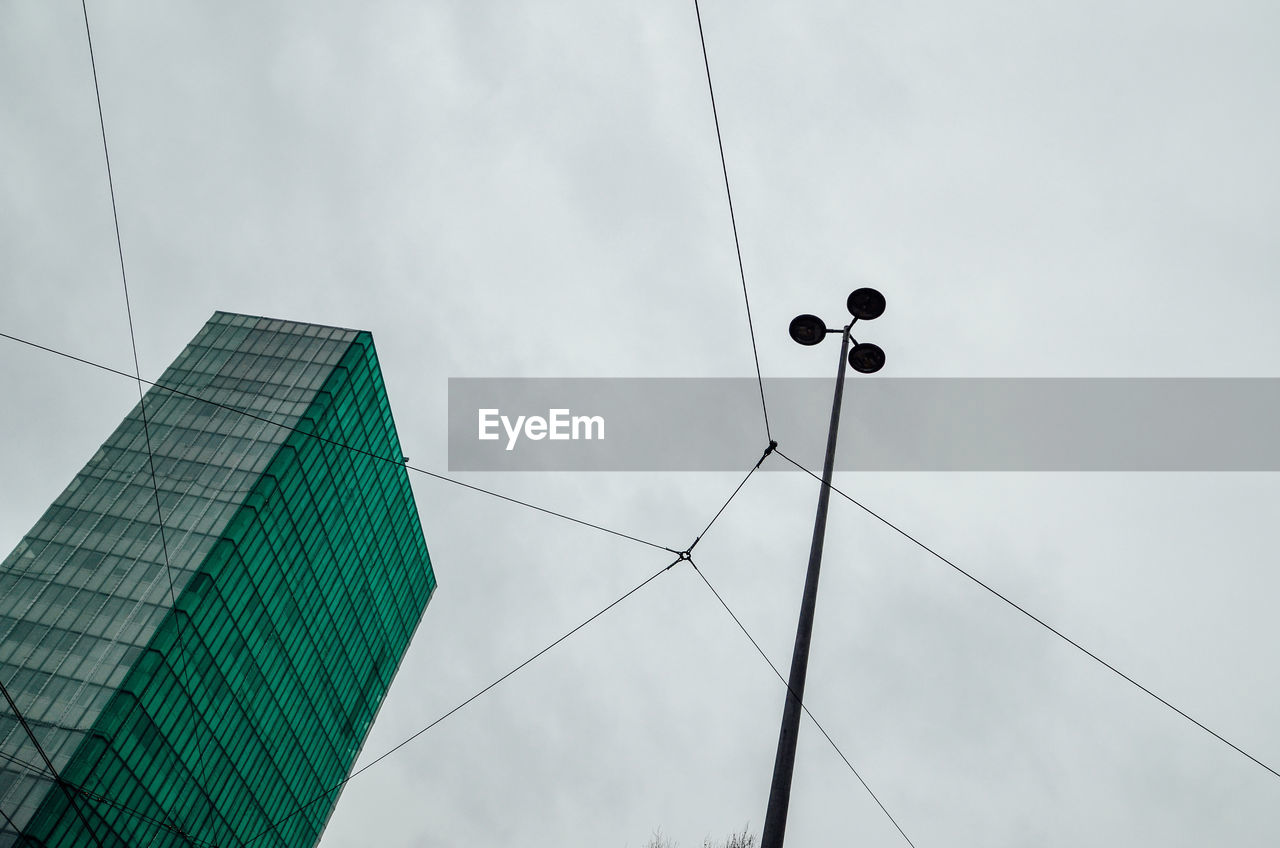 Low angle view of street light and cables with building against sky