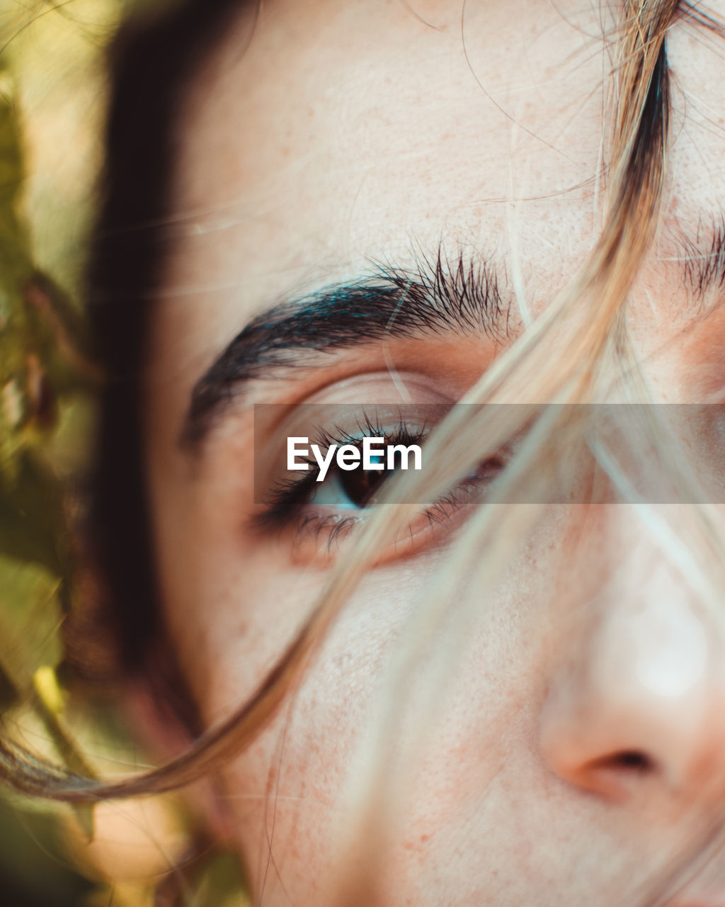 Closeup of crop young female with brown eyes looking at camera against green leaves in nature