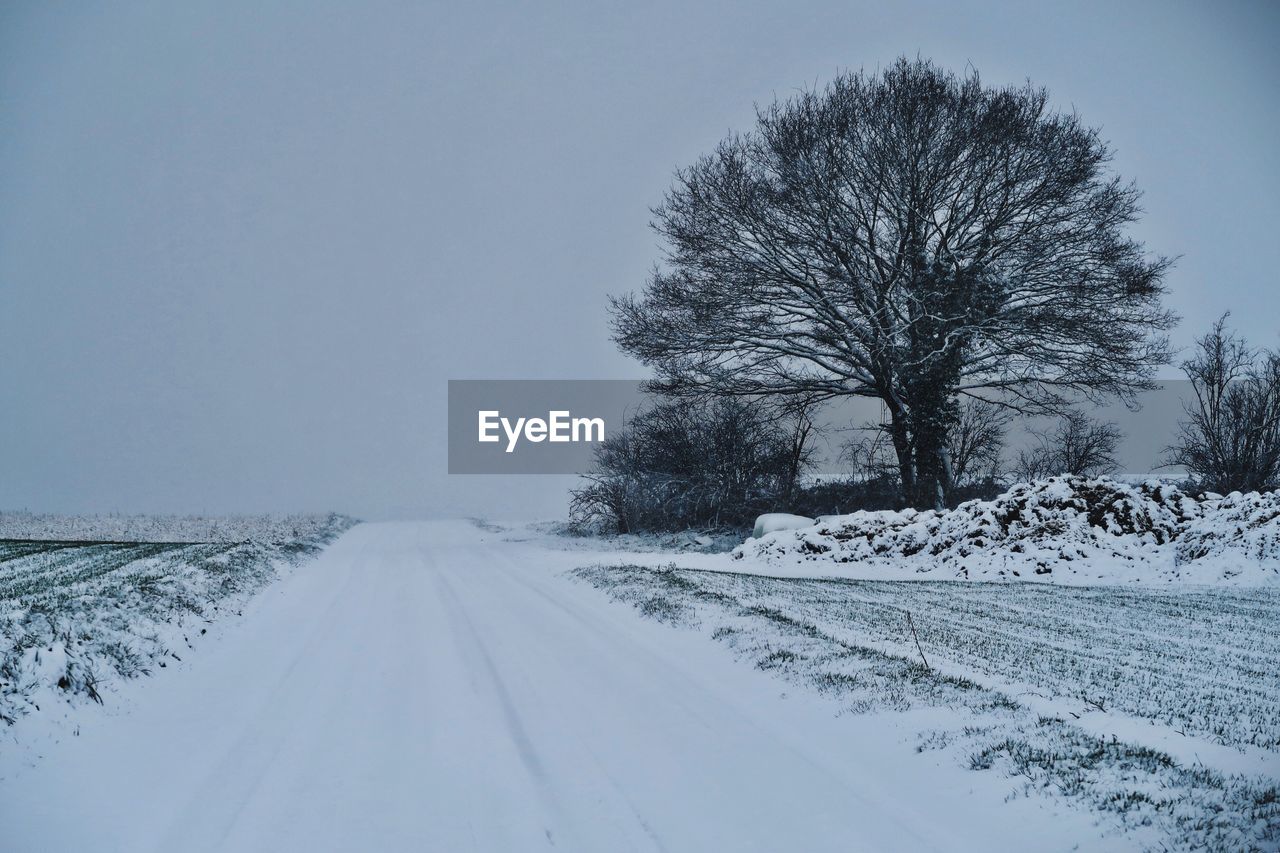 SNOW COVERED ROAD AMIDST FIELD AGAINST SKY