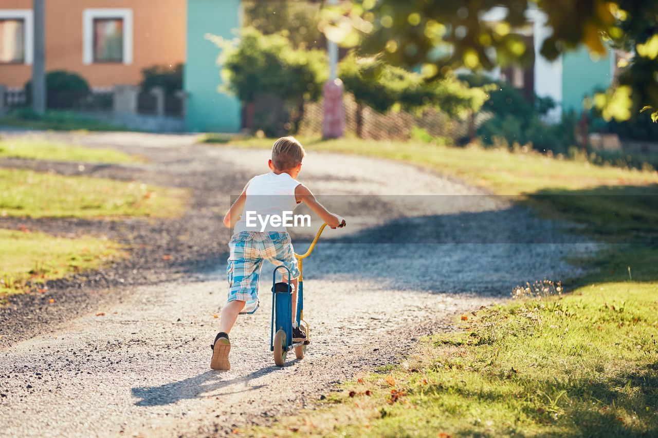 Rear view of boy playing with push scooter on road