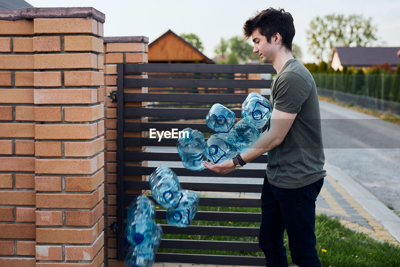 Young man throwing out empty used plastic water bottles into trash bin. collecting plastic waste